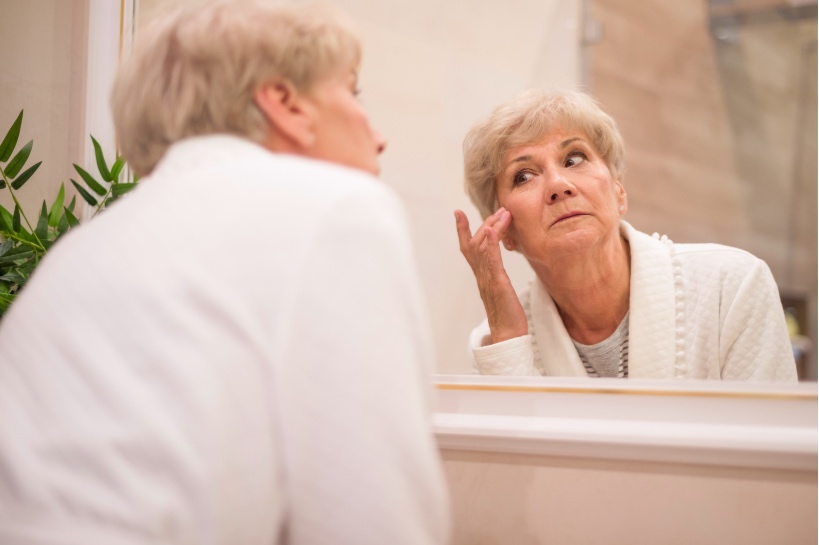 oudere vrouw kijkt in spiegel en trekt haar huid weer strak