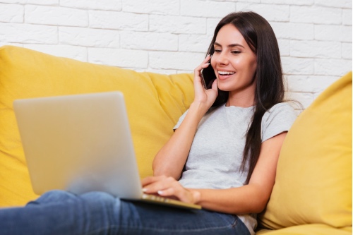 vrolijke bellende vrouw met laptop op bank